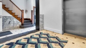 A hallway with a patterned rug, a wooden staircase, and a modern elevator.