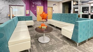 A modern waiting area with teal and white seating, a central table with a 'Give Thanks' sign, and a 'Chart Your Course' sign on the wall.