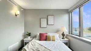 A hotel room with a bed, bedside tables, a lamp, a plant, and framed artwork on the wall. - Stay in the heart of downtown! Walk to Casey's Center, restaurants, and nightlife. Enjoy free parking and all the comforts of home. (Des Moines)