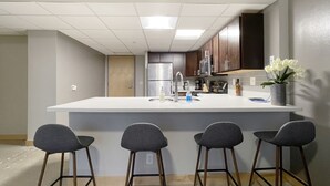 Une cuisine moderne dotée d’un grand îlot central, de tabourets de bar, d’appareils électroménagers en acier inoxydable et d’un vase rempli de fleurs.