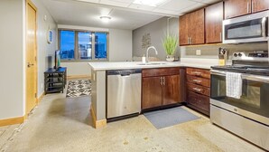 A modern kitchen with stainless steel appliances, wooden cabinets, and a view of the city through the window.