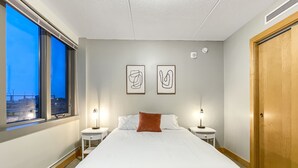 A hotel room with a large bed, two bedside tables with lamps, a window with a view, and a door.