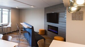 A modern lounge area with a bar, seating, a fireplace, and a flat-screen TV mounted on the wall.