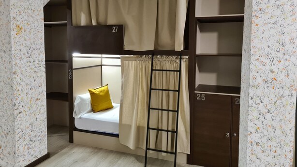 Habitación con literas, una escalera, almohada amarilla y colcha blanca.