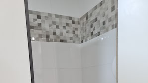Un baño pequeño y blanco con pared de ducha en cerámica, inodoro y piso de madera.