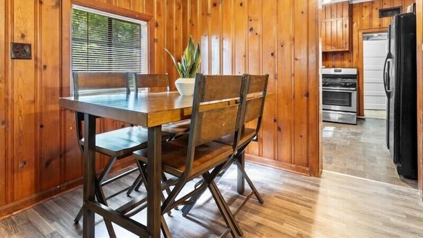 A wooden-paneled room with a dining table and chairs, a potted plant, and a kitchen area with appliances. - 1BR Residence With Vast Backyard (Des Moines)
