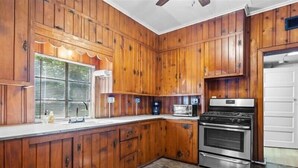 A kitchen with wooden cabinets, a stove, a microwave, and a sink. - 1BR Residence With Vast Backyard (Des Moines)