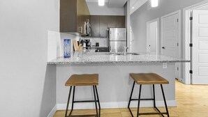 A modern kitchen with a granite countertop, stainless steel appliances, and two wooden stools. - Beautiful 2BR/2BA in Bldg connected to Skywalk (Des Moines)