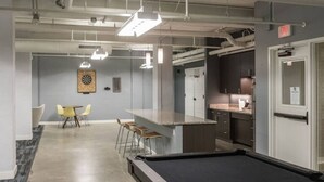 A modern kitchen with bar stools, a dartboard, and a pool table.