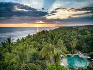 A tropical resort with a pool area surrounded by palm trees and a view of the ocean at sunset. - Clandestino Habitacion Queen 2 camas

 (Provincia de Puntarenas)