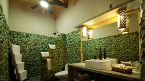 Un baño con pared de piedra, una escalera de madera, un lavabo blanco y un espejo con una lámpara.