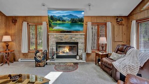 Ein gemütliches Wohnzimmer mit Kamin aus Stein, einem großen Flachbildfernseher darüber und einem bequemen Ledersofa.