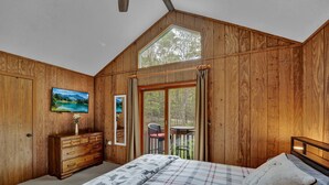 Ein Schlafzimmer mit Bett, Schminktisch, Fernseher und einem Fenster mit Vorhängen.