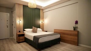 A modern bedroom with a bed, bedside tables, a wooden headboard, and a wall-mounted light fixture. - ATAKUM AYKA OTEL (Atakum)
