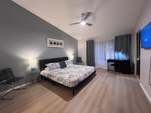 A bedroom with a bed, bedside lamps, a desk, a chair, a ceiling fan, and a TV.