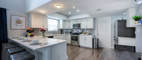 A modern kitchen with white cabinetry, a central island, and a dining area with a wooden table.