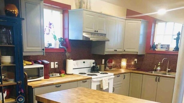 Een keuken met een houten tafel, twee barkrukken, een fornuis, magnetron en kastjes.
