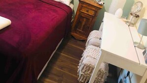 Een slaapkamer met een bed, nachtkastje, bureau en wandtapijt.