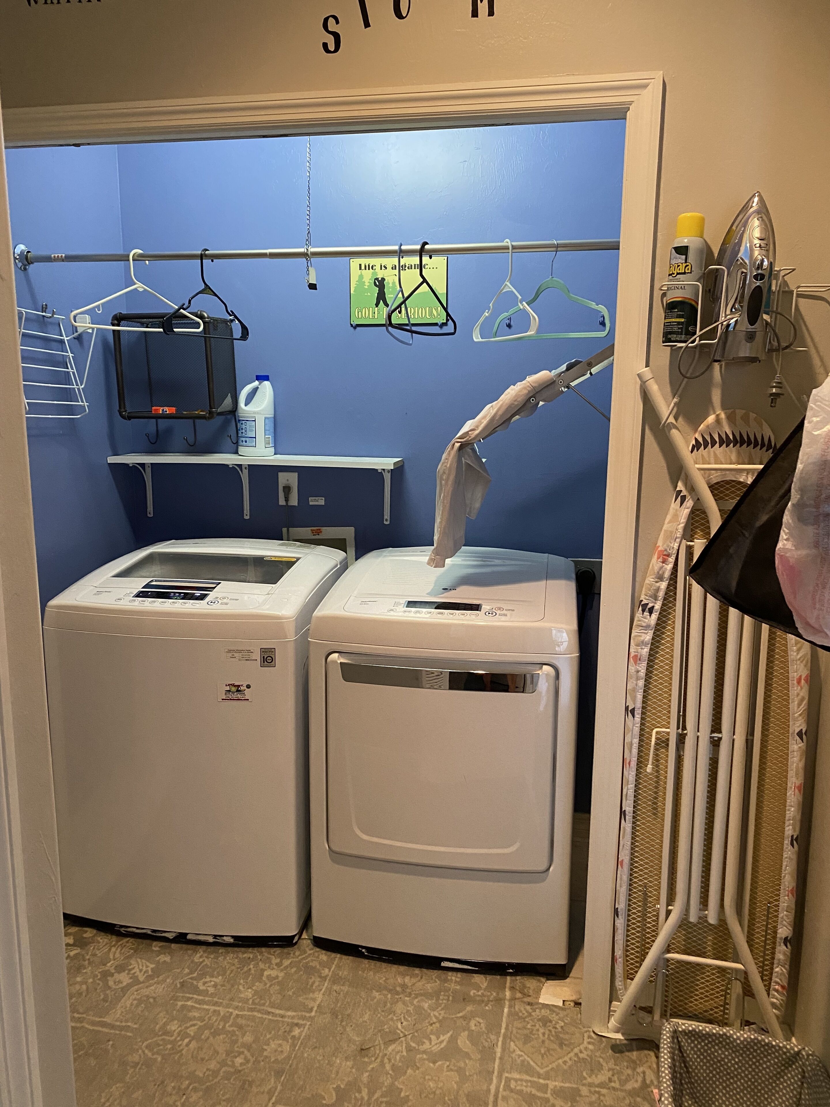 A laundry room with two front-loading washing machines, a drying rack, and a wall-mounted ironing station.