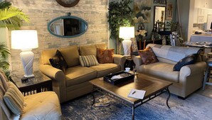 A living room with a sofa set, coffee table, and lamps. There is a clock on the wall and a mirror above the sofa. - Golf Excellence! Make it yours! Available Nov-Dec 20. (Naples)