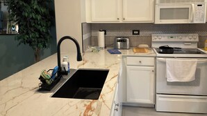A kitchen with white cabinets, a black sink, a microwave, and an oven. - Golf Excellence! Make it yours! Available Nov-Dec 20. (Naples)