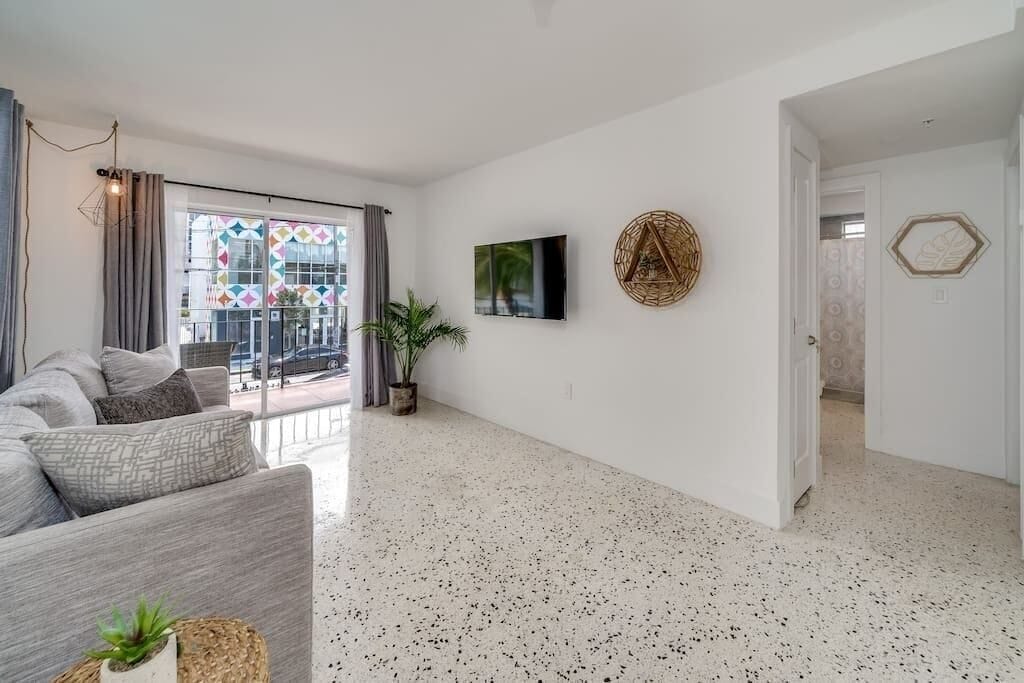 Un salon moderne avec un canapé gris, une plante en pot et un téléviseur fixé au mur.