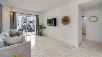 Un salon moderne avec un canapé gris, une plante en pot et un téléviseur fixé au mur.