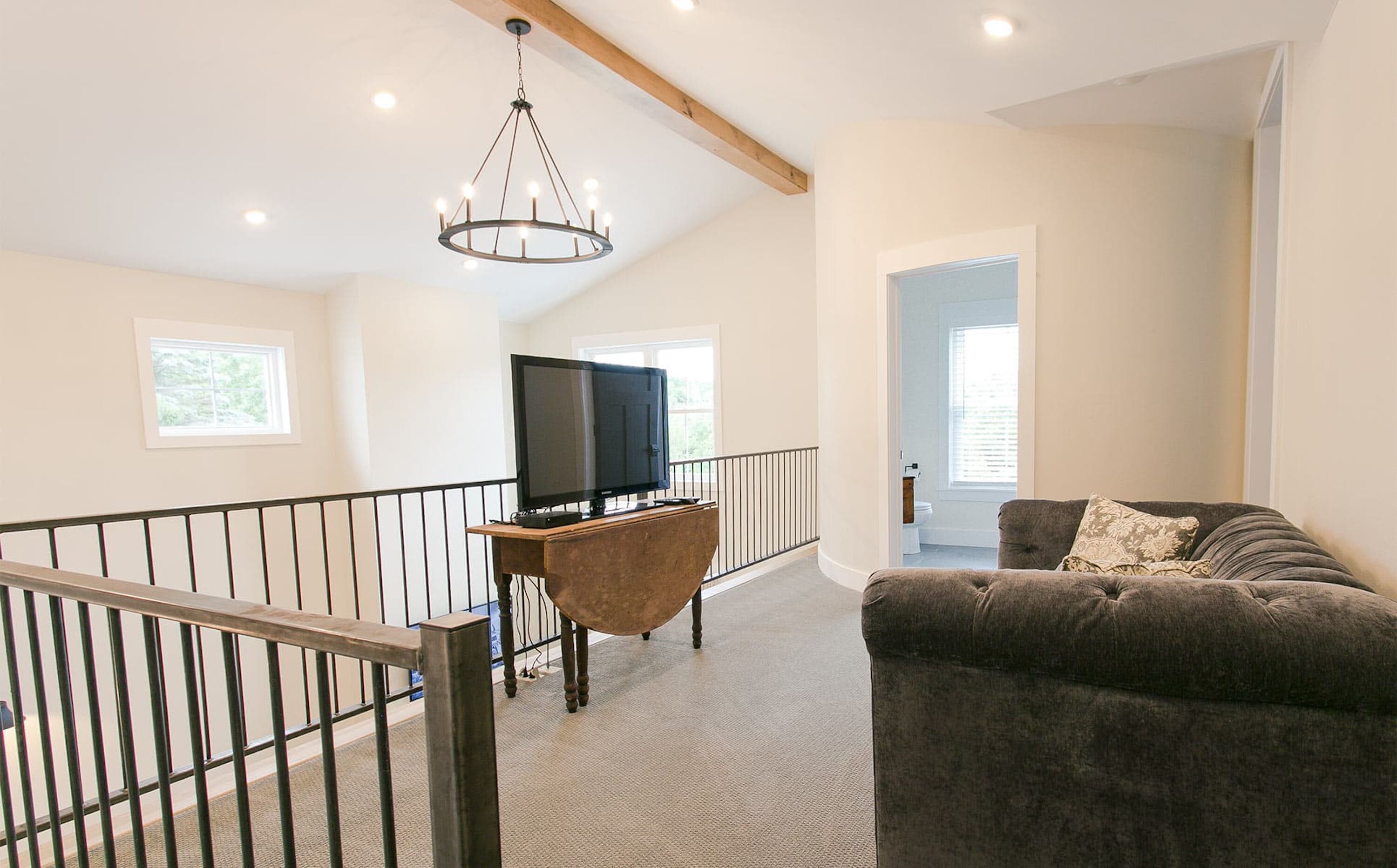 A spacious living area with a large flat-screen TV on a wooden stand, a grey sofa, and a chandelier.