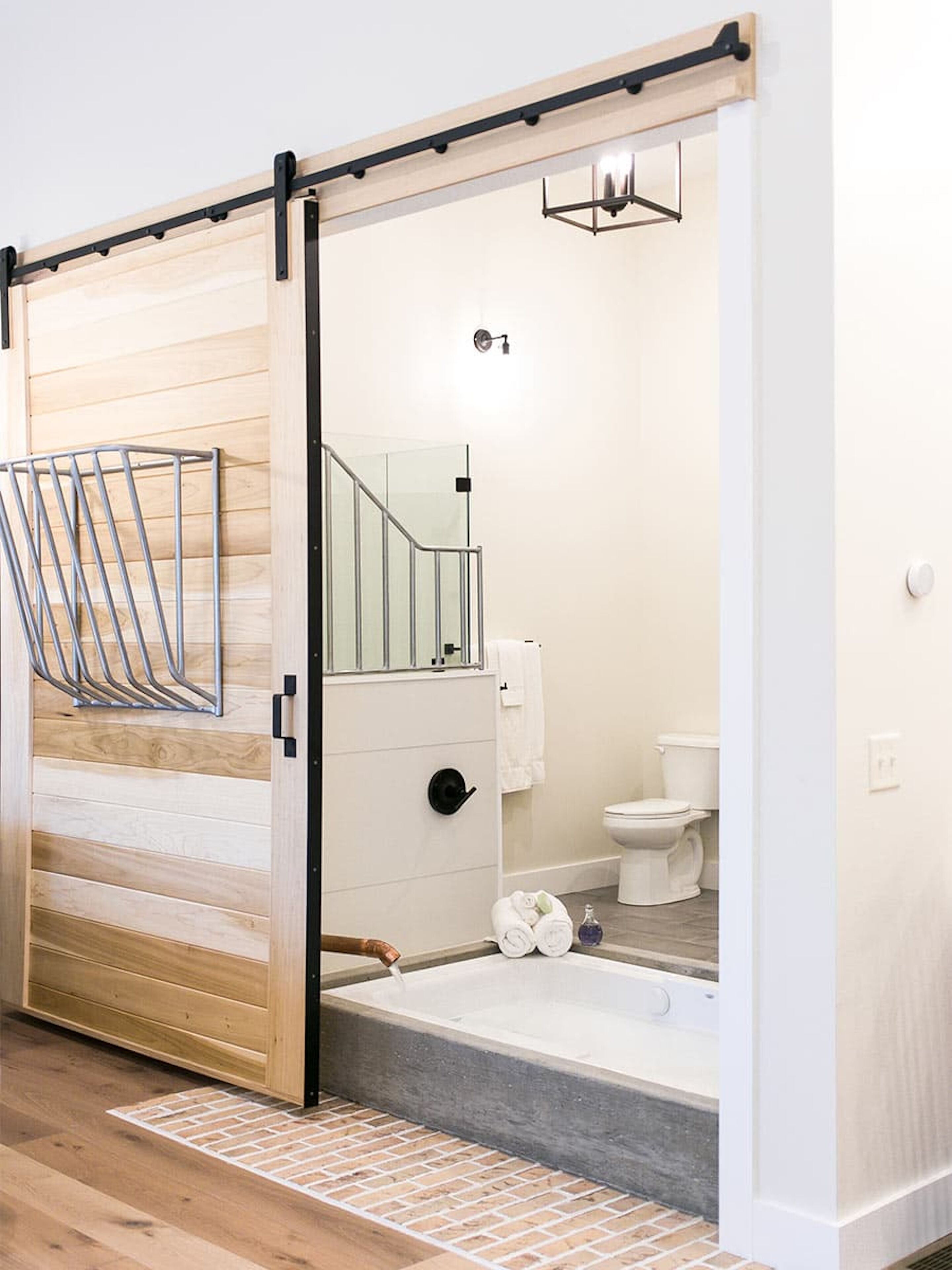 Un baño moderno con puerta corredera de madera, cabina de ducha de cristal, inodoro y bañera.
