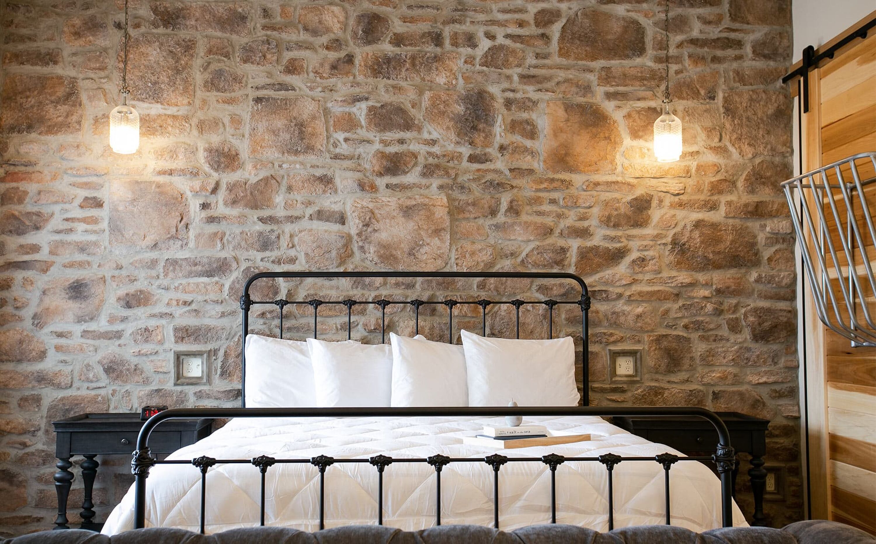 Un letto con struttura in metallo, biancheria da letto bianca e una parete in pietra sullo sfondo.