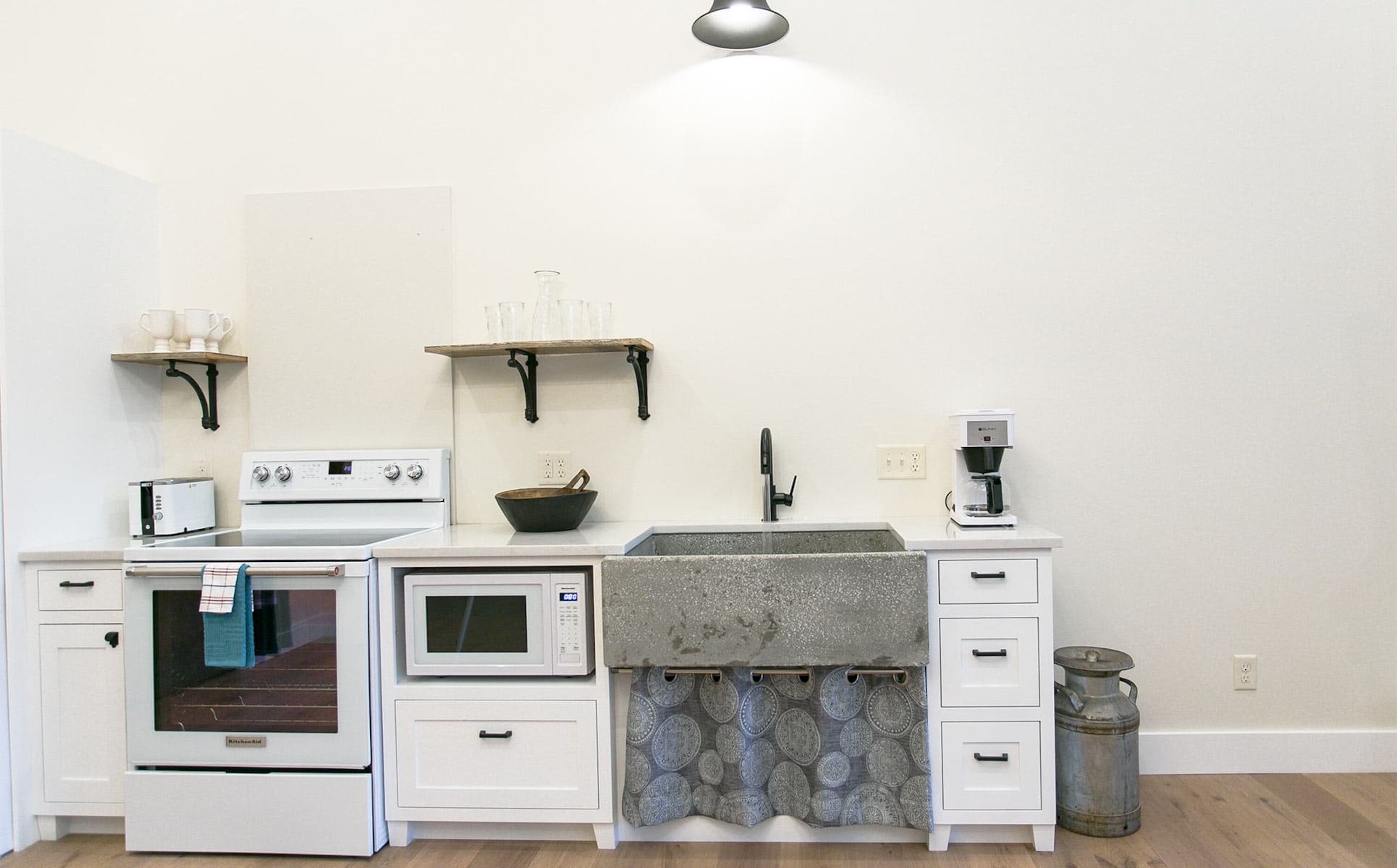 Une cuisine avec des meubles blancs, une cuisinière, un four à micro-ondes, une machine à café et un porte-casseroles suspendu.
