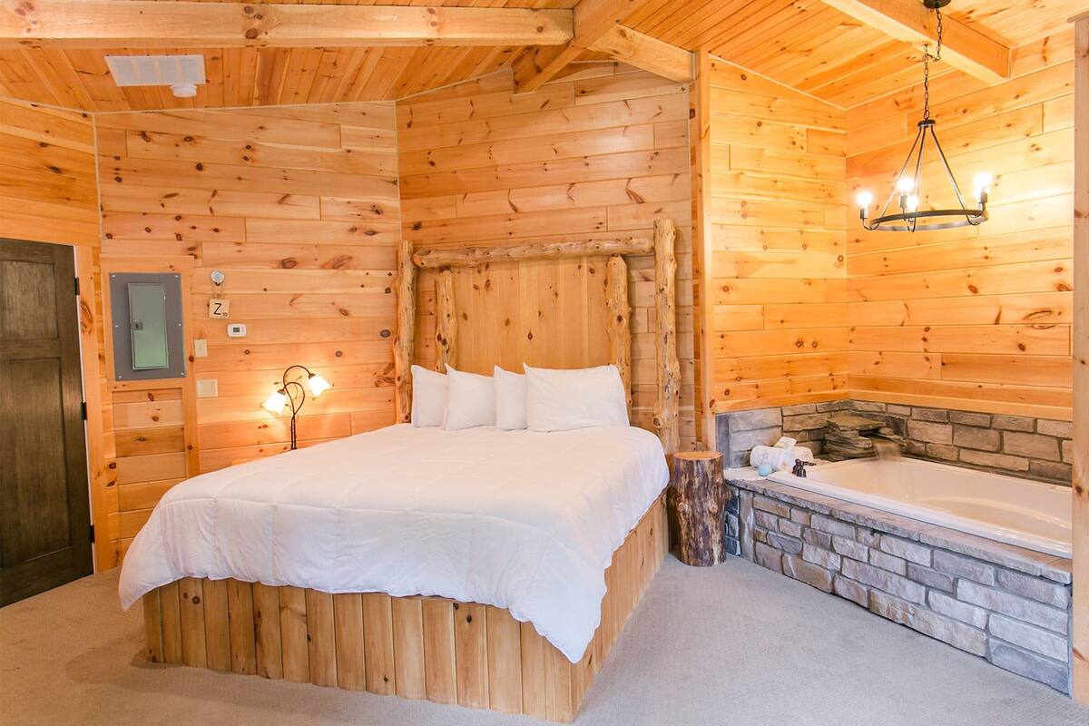 A wooden cabin room with a bed, a stone fireplace, and a wooden bench.