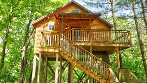 A wooden cabin with a balcony and a staircase, surrounded by trees. - Pine Cove Treehouses & Cabins (Millersburg)