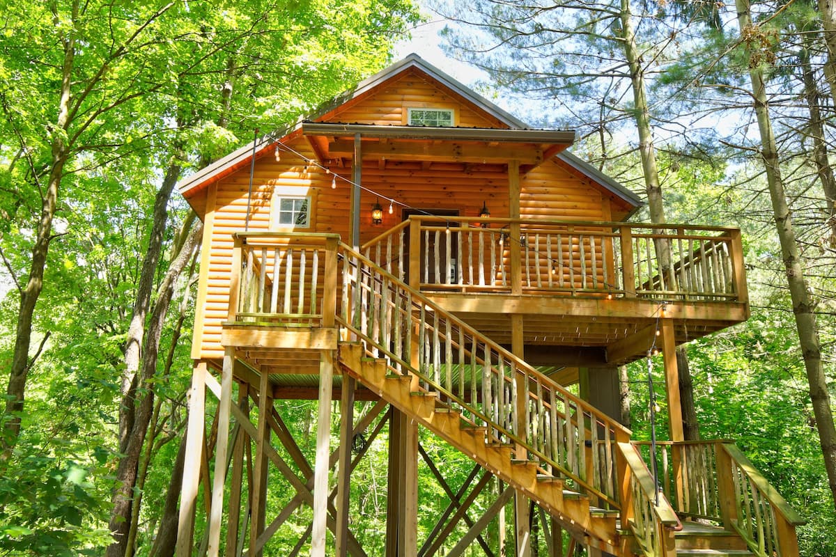 A wooden cabin with a balcony and a staircase, surrounded by trees.