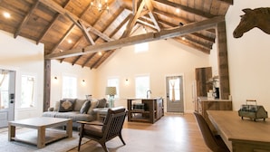 A spacious loft with exposed wooden beams, a loft bed, a dining table, and a kitchen area. - Pine Cove Treehouses & Cabins (Millersburg)