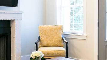 Een woonkamer met een gele fauteuil, een houten salontafel, een grijze bank en een open haard.