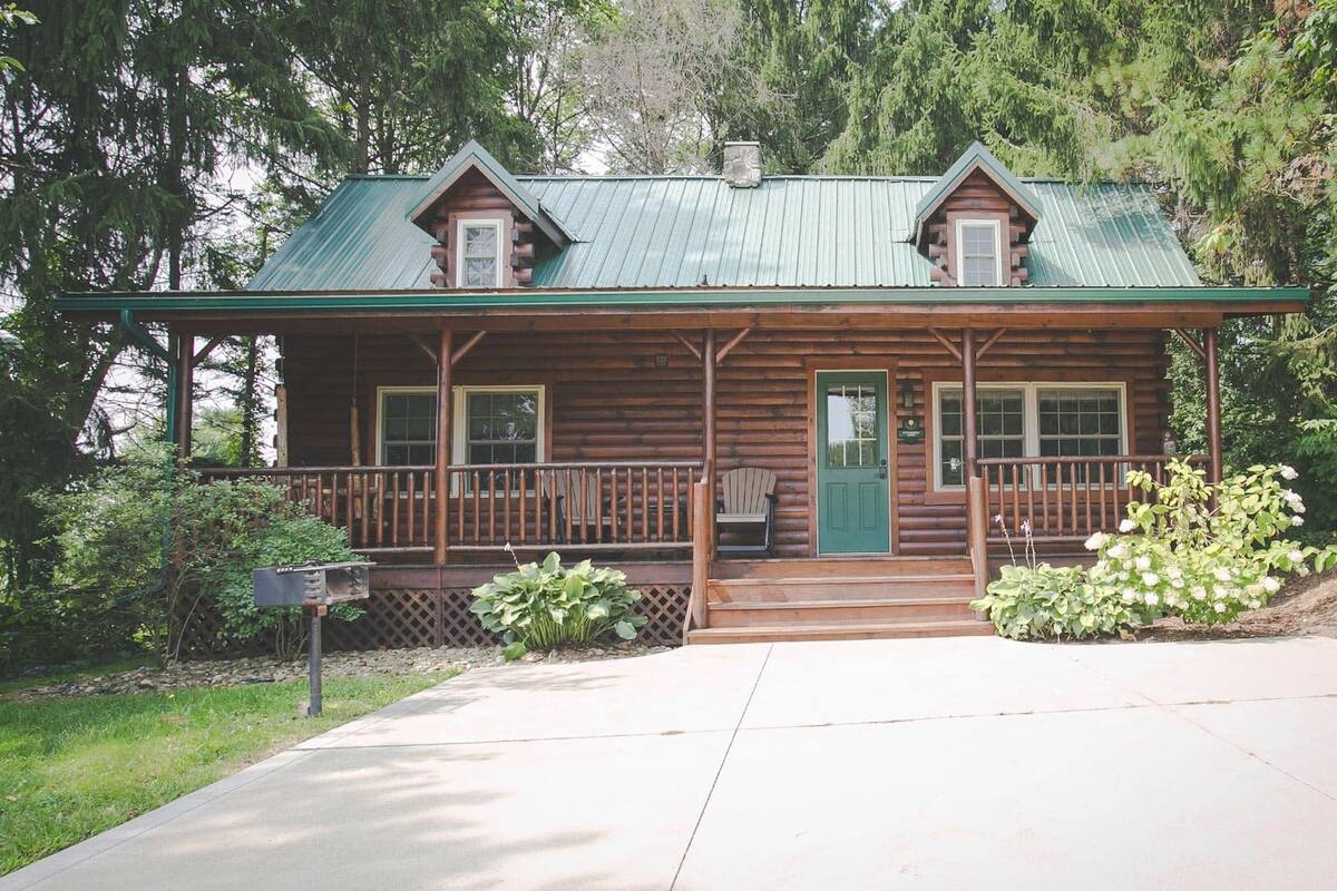 A log cabin with a green metal roof, a front porch, and a green door.