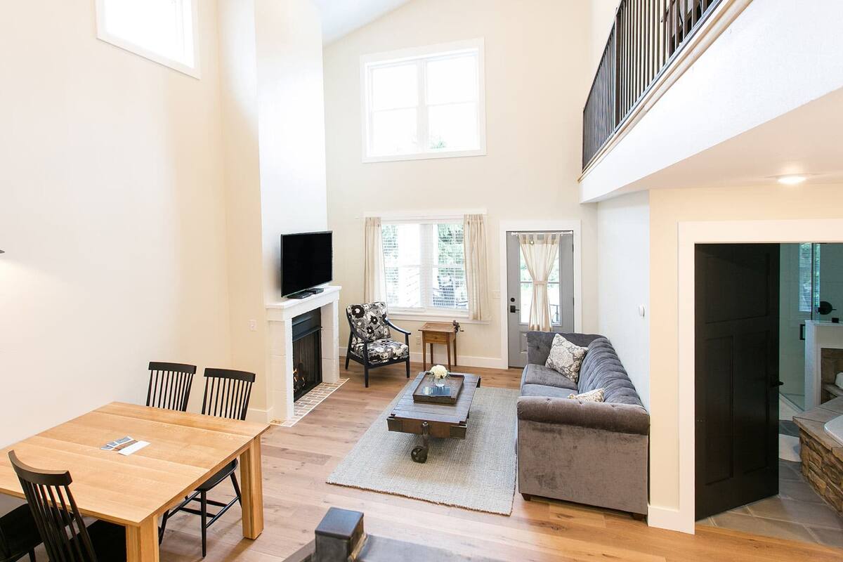 A spacious living area with a wooden dining table, chairs, a sofa, and a TV mounted on the wall.