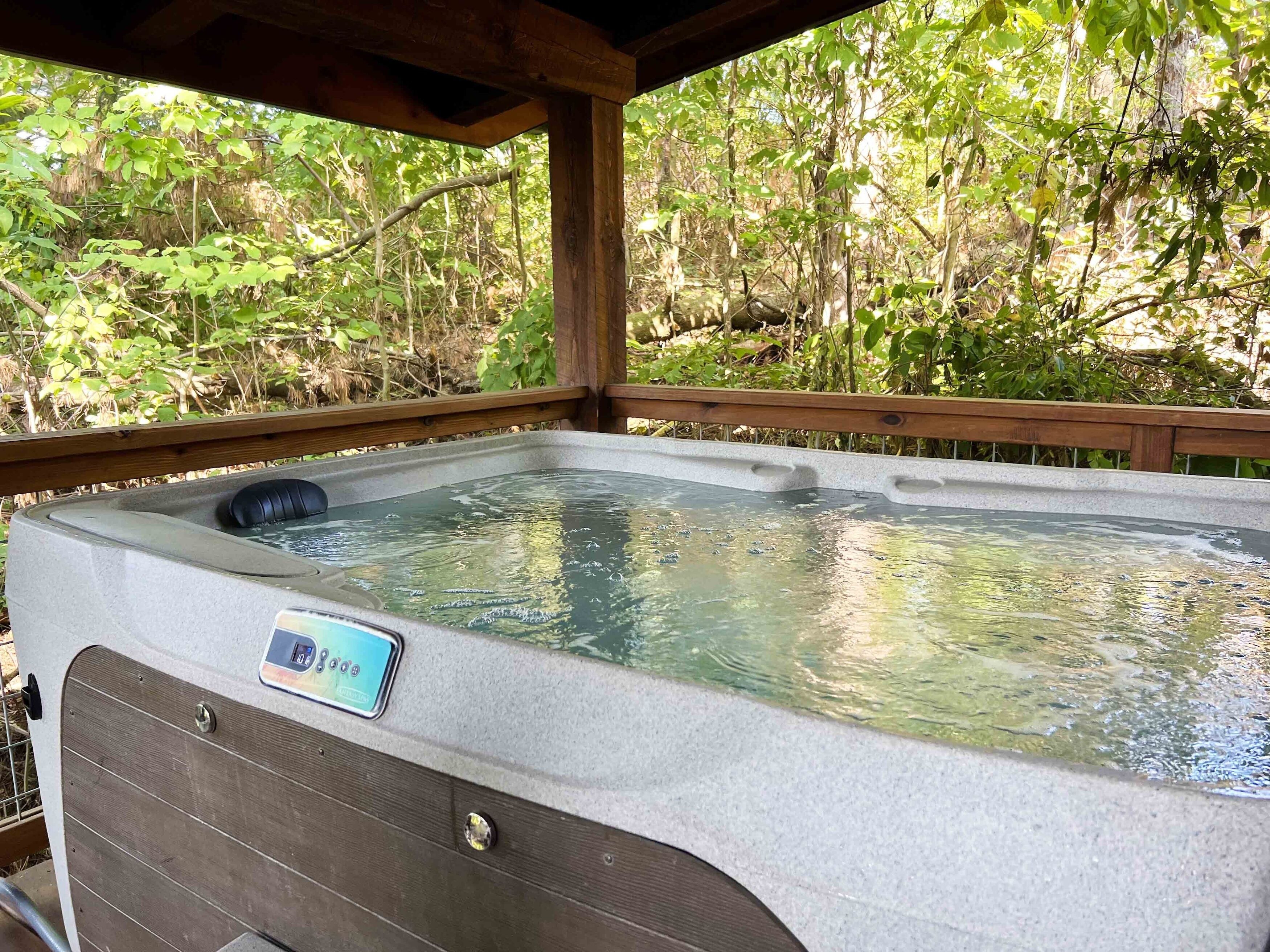 Un jacuzzi con pantalla digital de temperatura, rodeado por una terraza de madera y abundante vegetación.