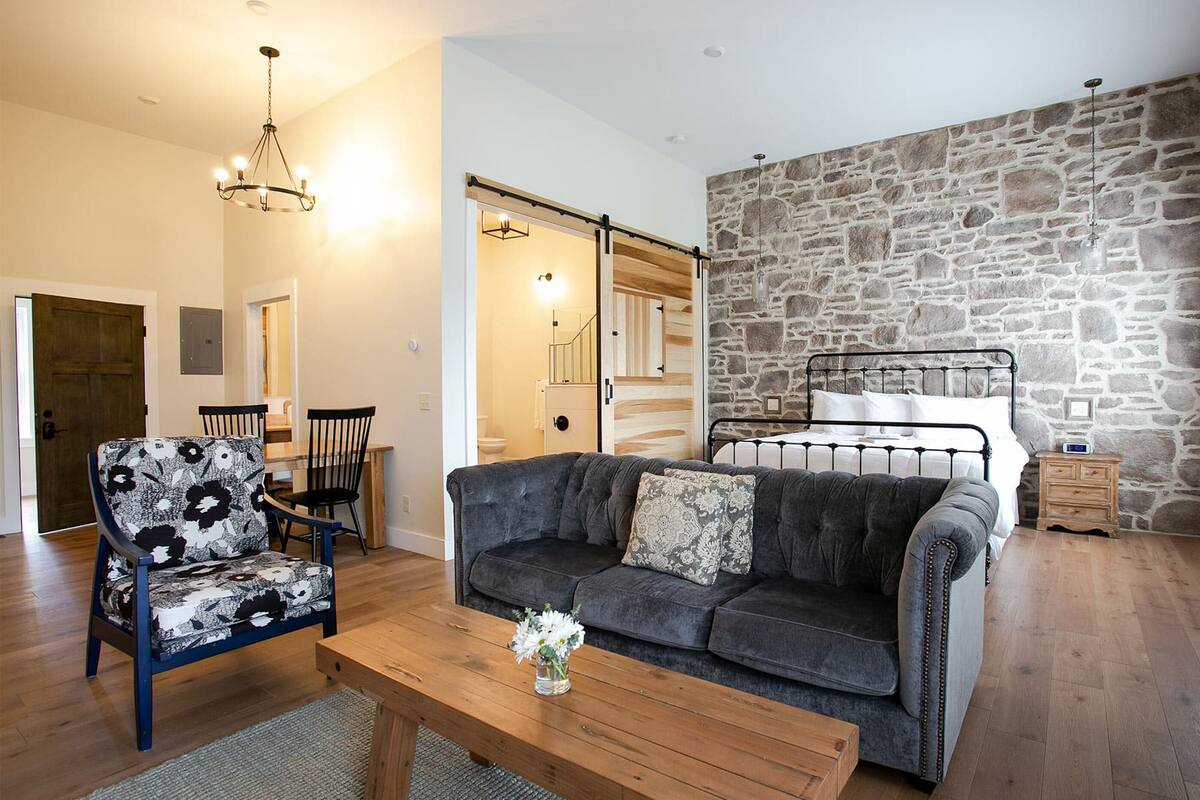 A cozy living room with a sofa, a chair, a wooden coffee table, and a stone wall.