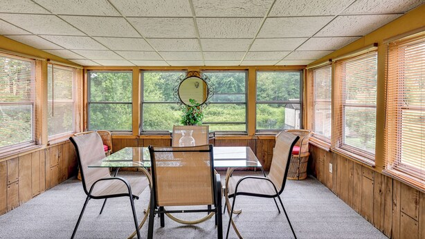 A sunroom with a glass table, four chairs, a mirror, and a potted plant. - Vintage Windsor Home: Private Yard & Covered Deck (Windsor)
