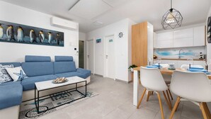 Ein modernes Wohnzimmer mit einem blauen Sofa, einem Essbereich mit weißen Stühlen und einer Küche mit weißen Schränken.