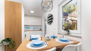 Ein moderner Essbereich mit einem Holztisch, gedeckt für vier Personen, weißen Stühlen und einem Fenster mit Blick auf Bäume.