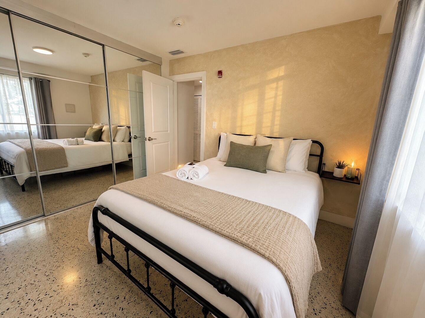 Une chambre d’hôtel avec un grand lit, un miroir, une table de chevet avec une lampe et une vue sur une autre chambre.