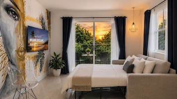 Une chambre avec un lit, un canapé, une télévision, un tableau et un balcon avec vue.