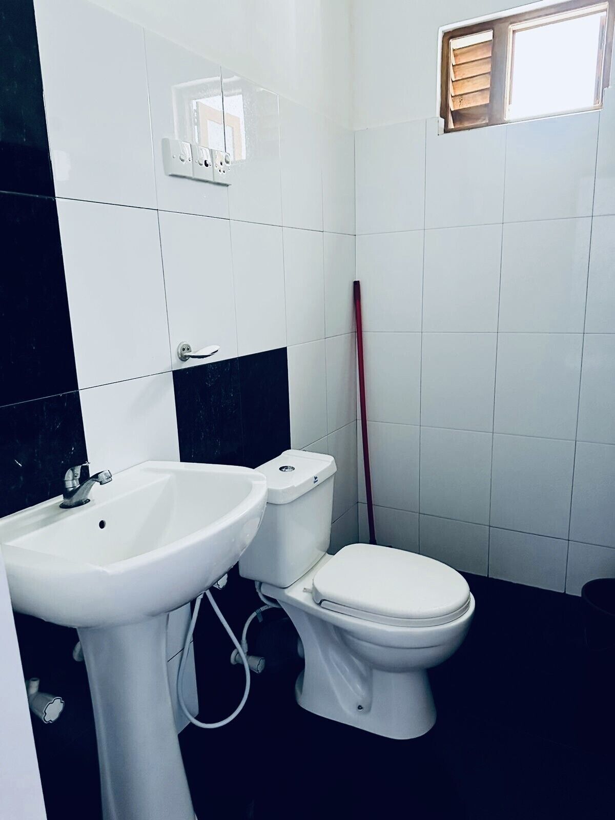 Une salle de bain avec un lavabo blanc, des toilettes et une fenêtre avec des stores.