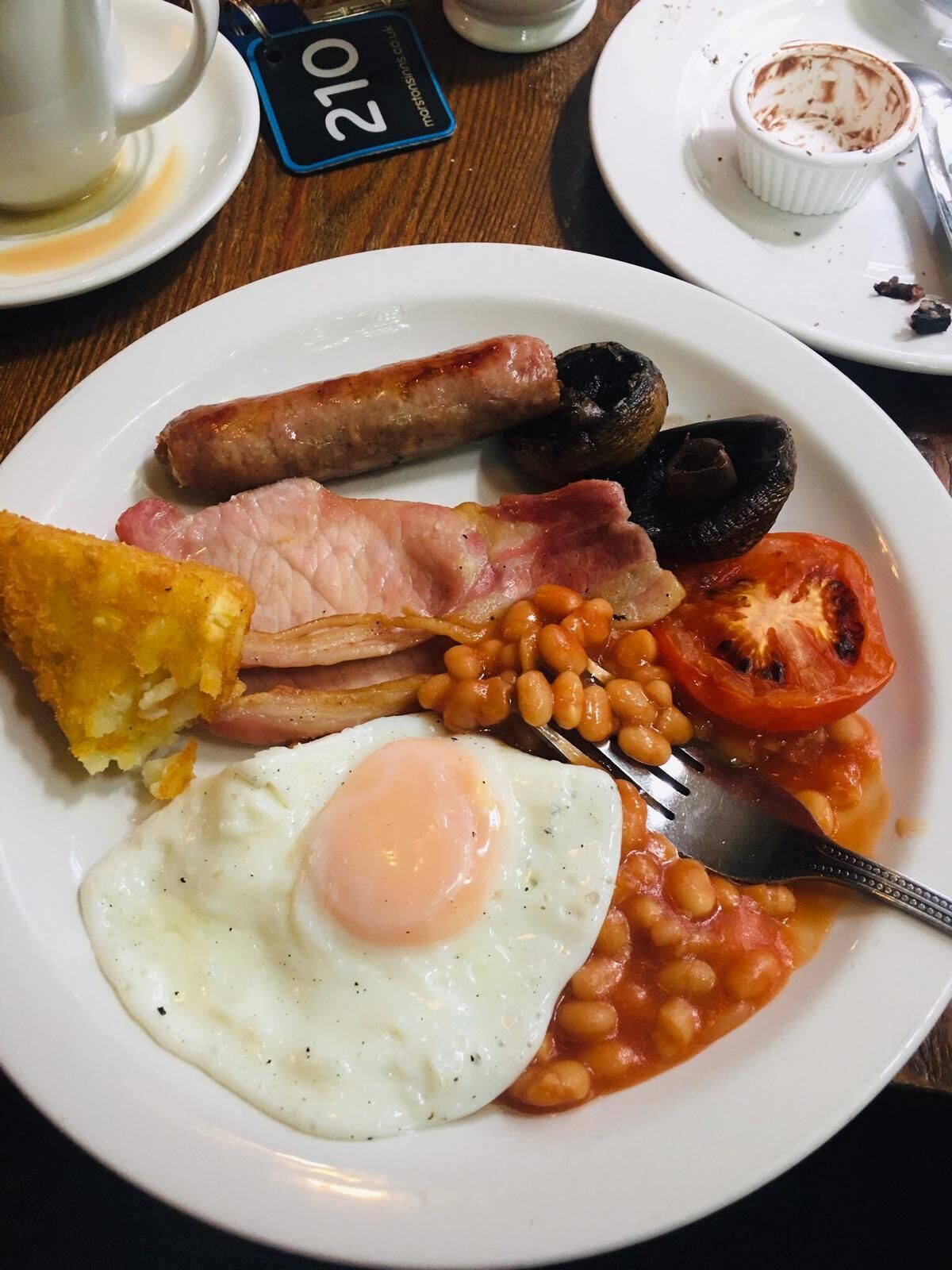 A plate of breakfast food including sausages, bacon, eggs, beans, and a tomato.