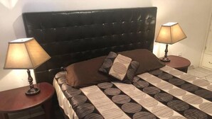 Une chambre à coucher avec une tête de lit capitonnée, deux tables de chevet avec des lampes, une couvre-lit à motifs et un coussin marron.