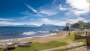 A beach with boats, a wooden walkway, and mountains in the background.