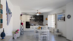 A modern kitchen with white cabinets, a dining area with white chairs, and a ceiling fan.
